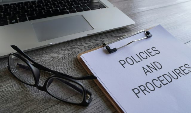 Paper clipboard with text POLICIES AND PROCEDURES on table